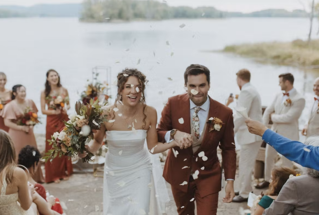 A bride and groom exit their wedding ceremony on the river with confetti sprinkled around.